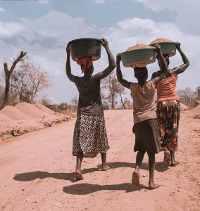 three women carrying basin while walking barefoot